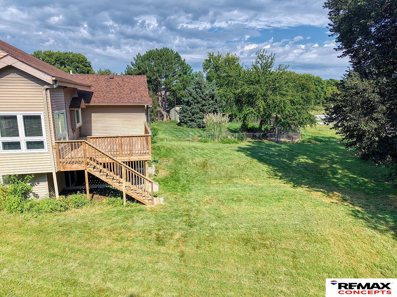 Home’s raised wooden deck and stairs overlook a spacious lawn bordered by mature trees.
