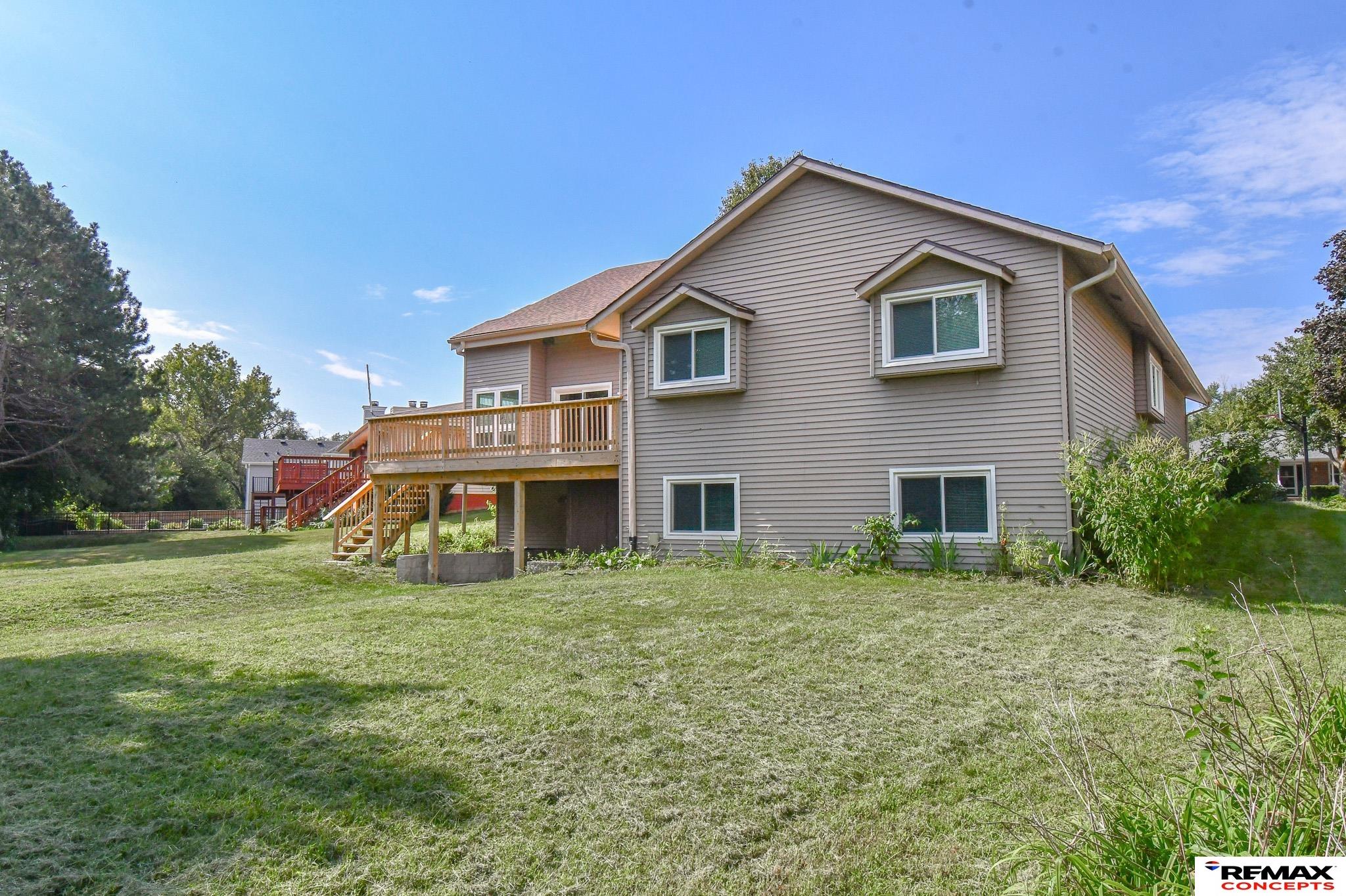 Rear of a gray two-story home with a raised wooden deck overlooking a broad lawn.