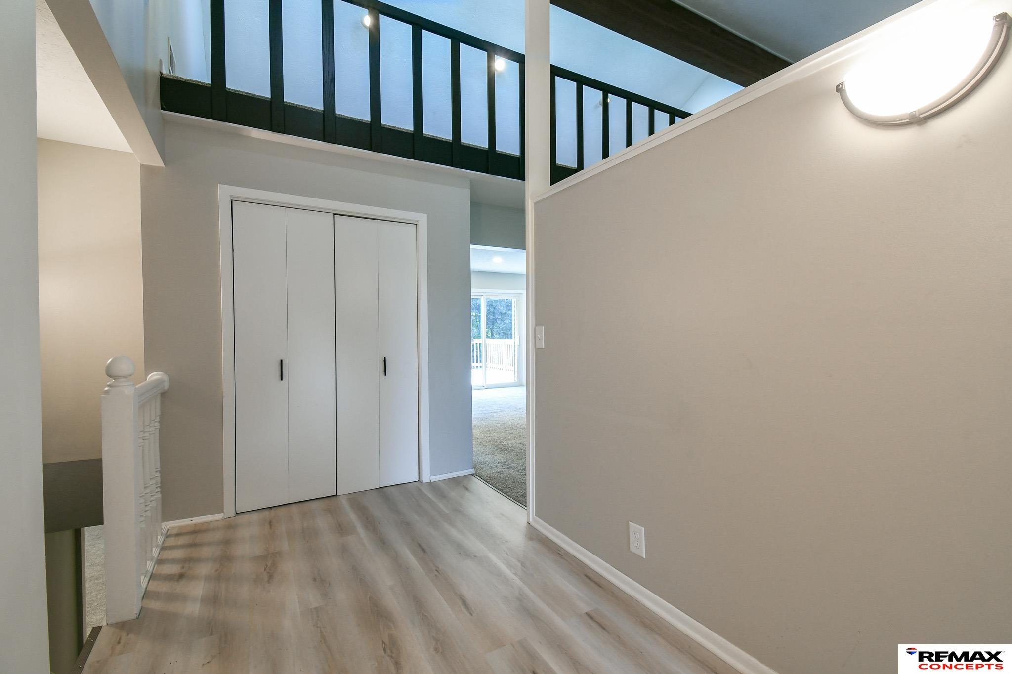 Entry hall with light wood-look flooring, white closet doors, and an open loft railing.