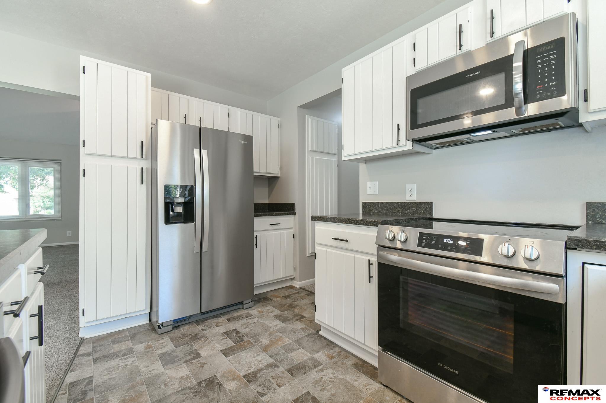 Kitchen with white cabinets, stainless steel appliances, dark counters, and patterned tile flooring.