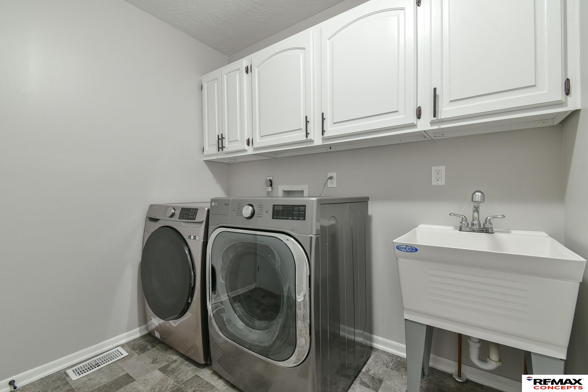 Laundry room with front-loading washer and dryer, utility sink, and white upper cabinets.