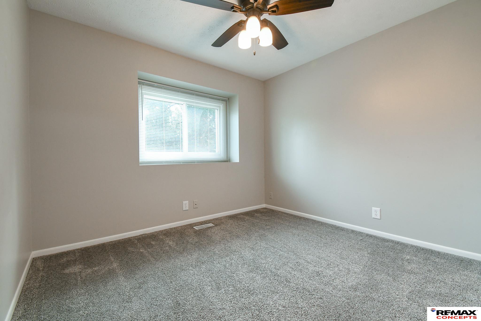 Empty carpeted bedroom with a recessed window and ceiling fan with lights.