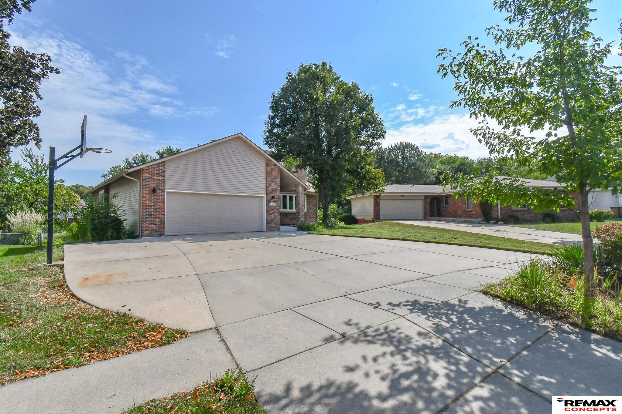 House with brick accents, attached double garage, wide driveway, and basketball hoop.