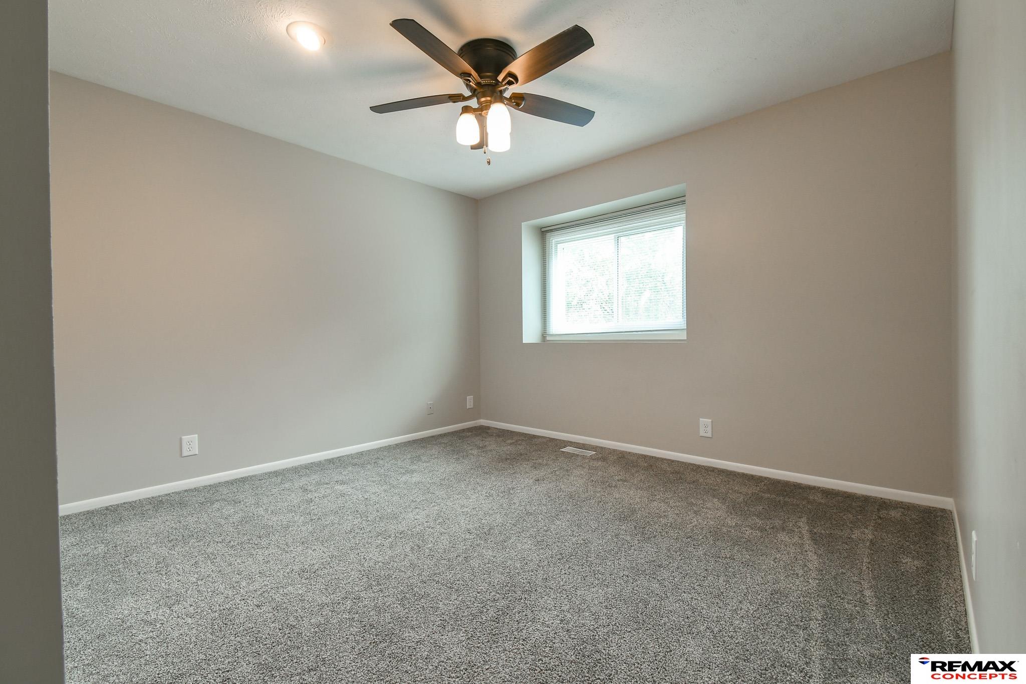 Empty carpeted bedroom with a ceiling fan and a window with blinds.