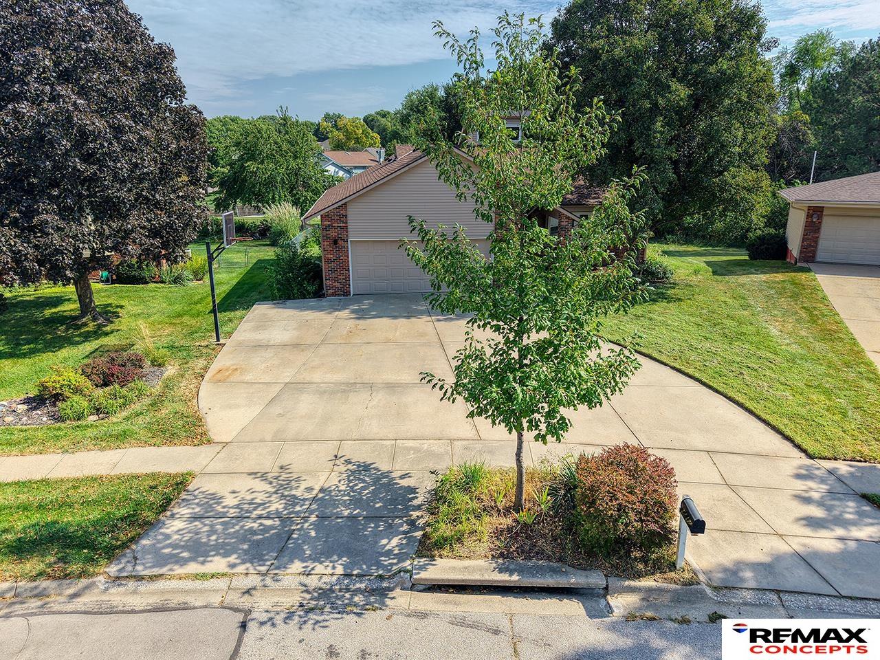 House with a two-car garage and broad driveway, partly obscured by a leafy tree.