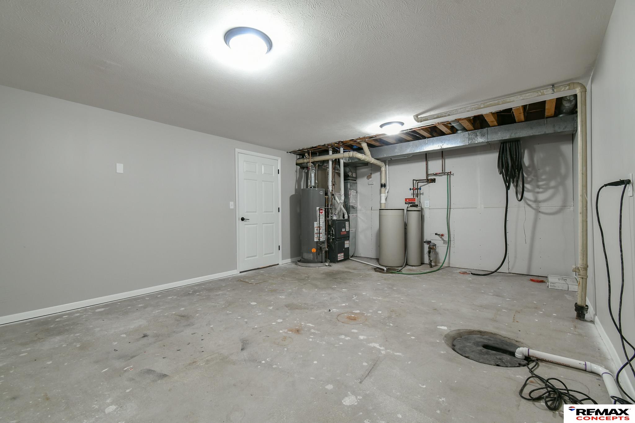 Basement utility room with a water heater, furnace, water treatment tanks, and floor drain.