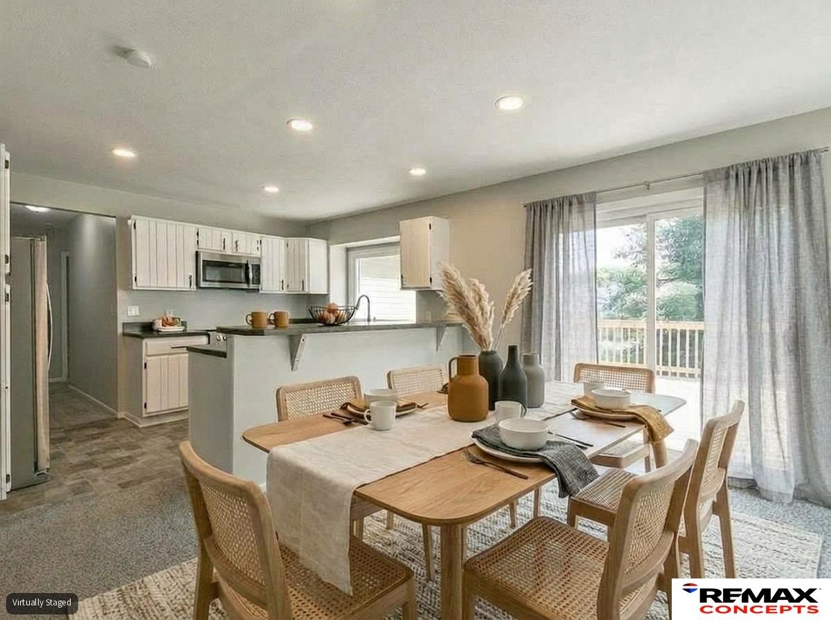 Open-plan kitchen and dining area with white cabinets, a wood table, and a large window overlooking a deck.