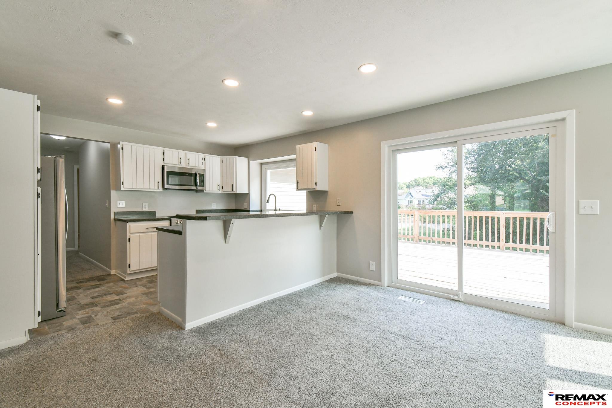 Open kitchen and carpeted living area with white cabinets and sliding doors to a deck.