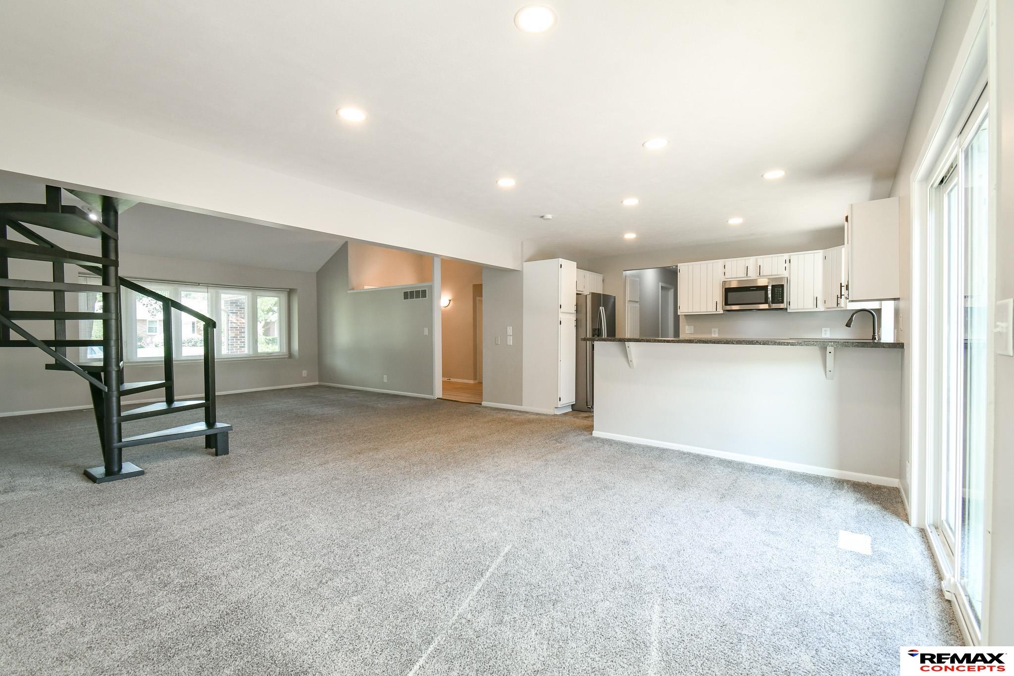 Open-plan living area and kitchen with a black spiral staircase and sliding glass doors.