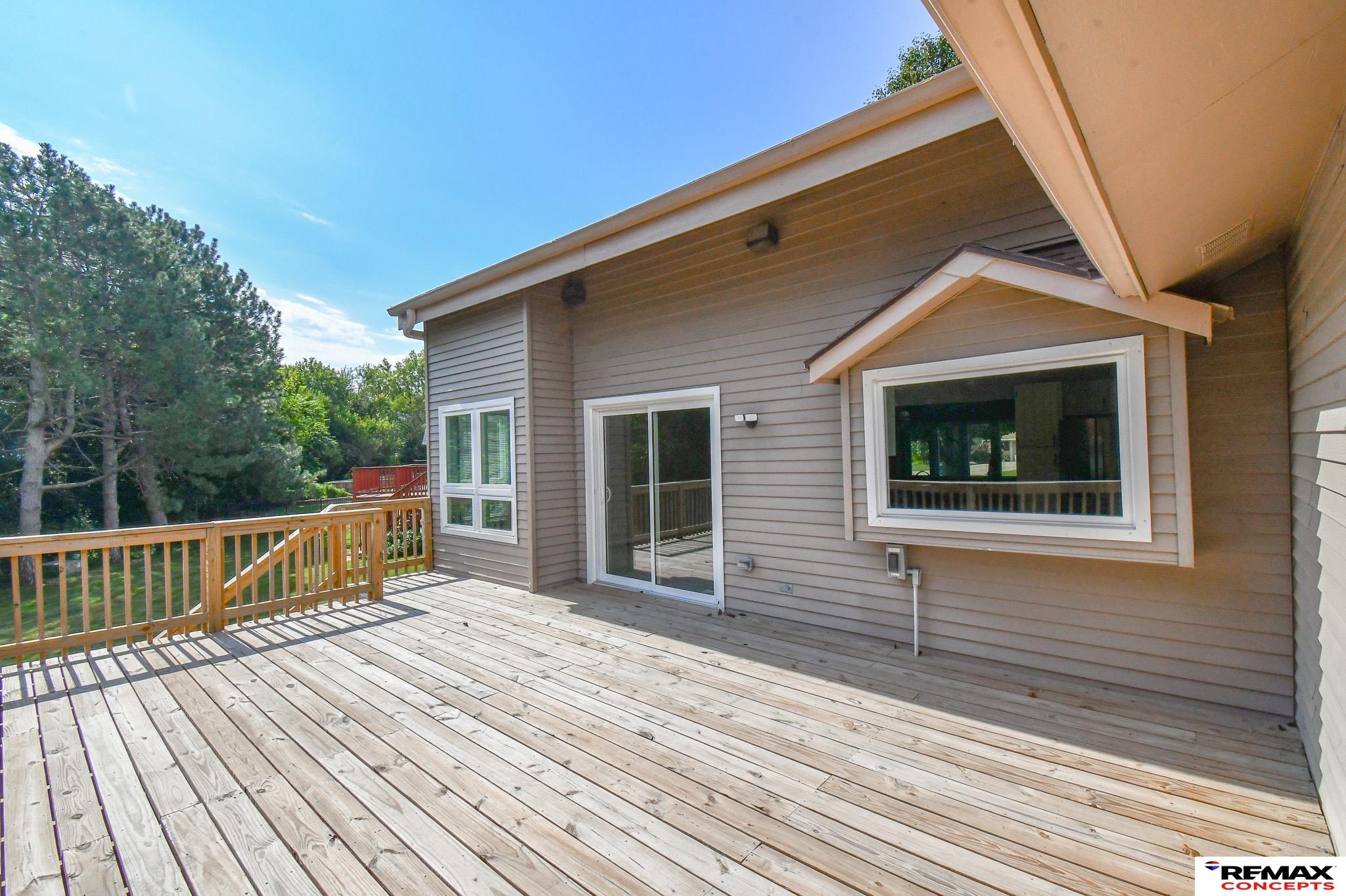 Wooden deck beside a gray-sided home, with a sliding glass door and trees beyond the railing.