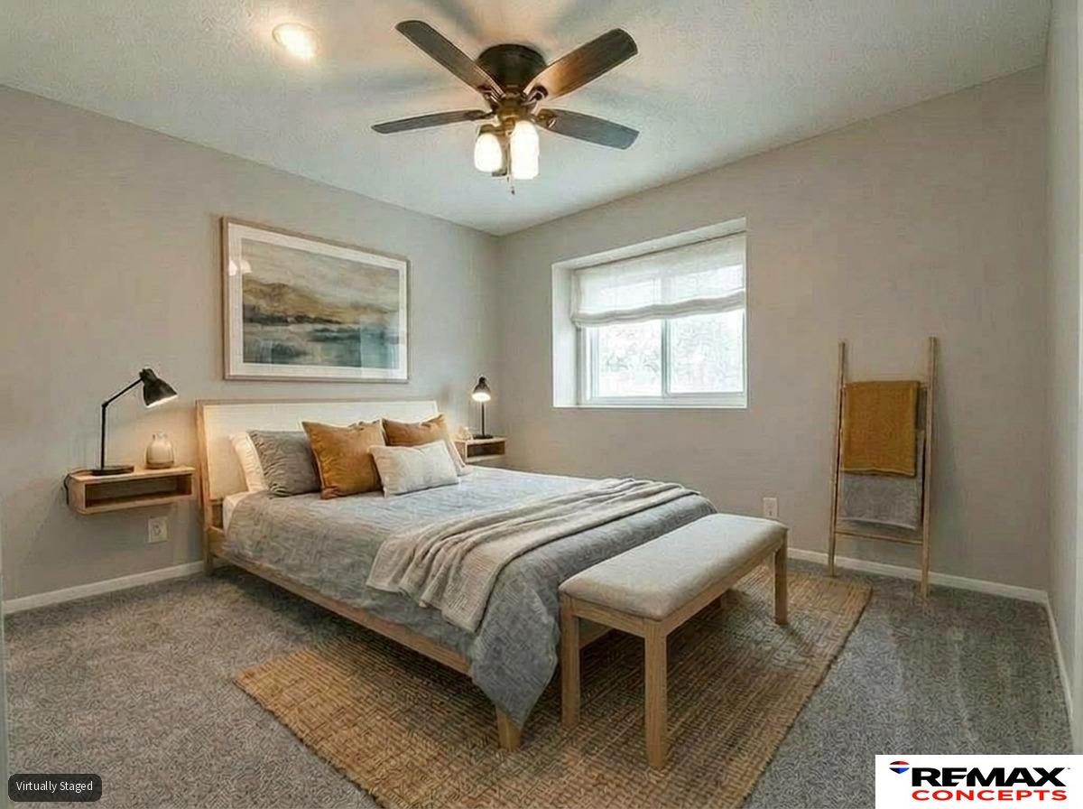 Staged bedroom with gray bedding, mustard accent pillows, a window, and a cushioned bench at the foot of the bed.