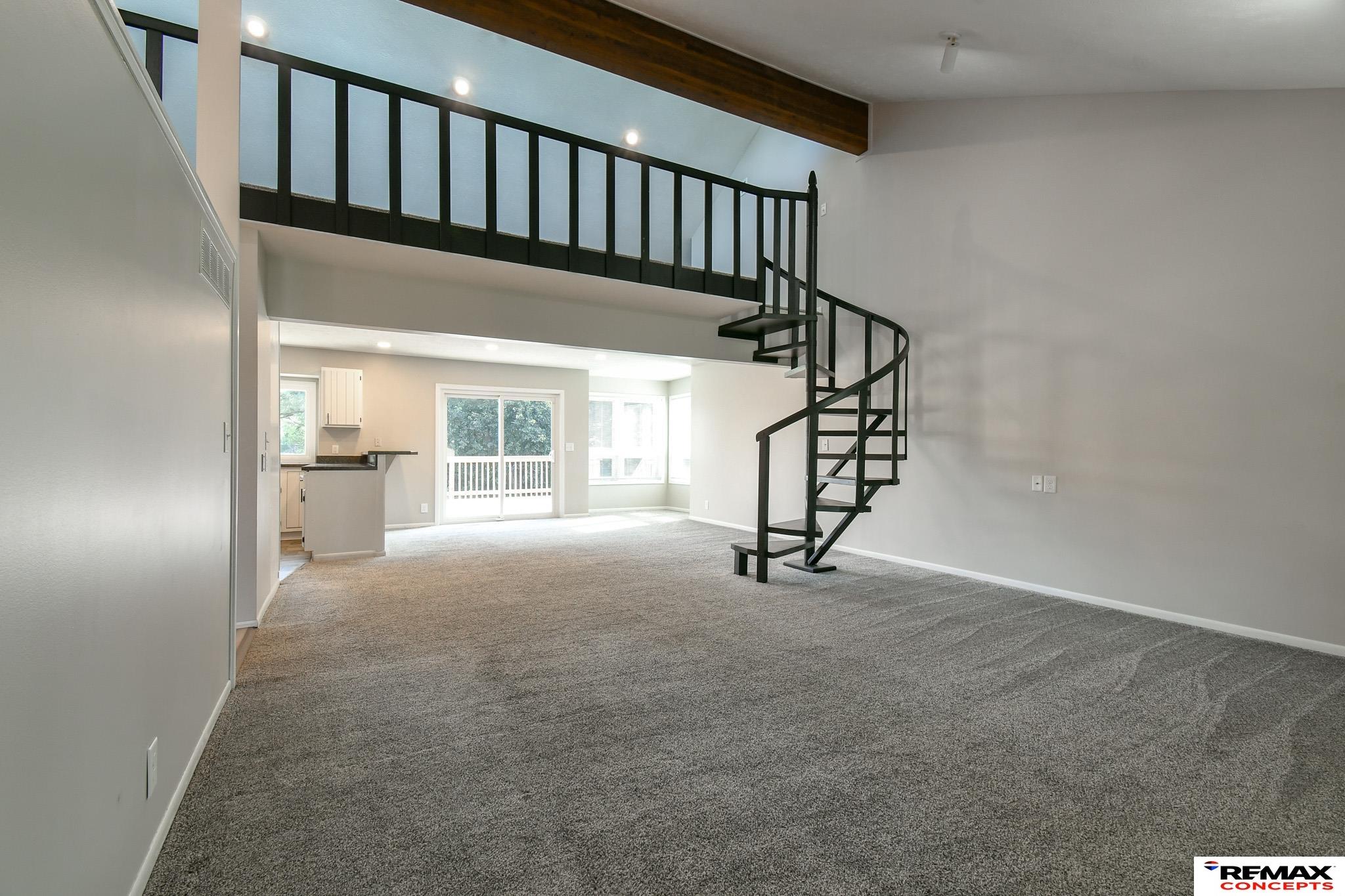 Empty living room with a black spiral staircase leading to an open loft.