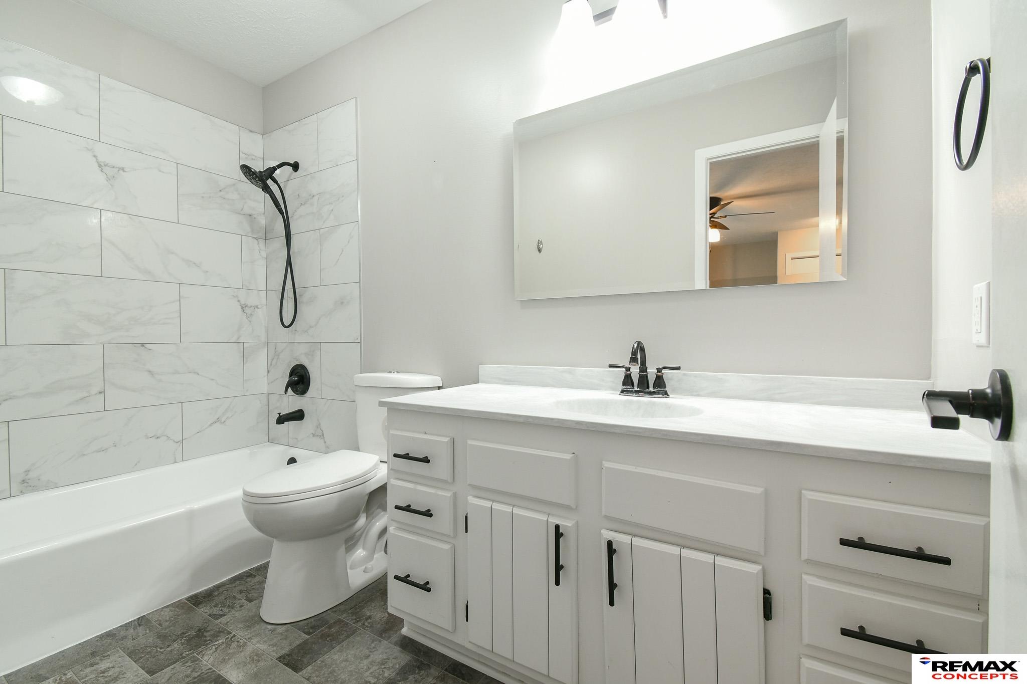 Bathroom with marble-look shower tile, white vanity, and black fixtures.