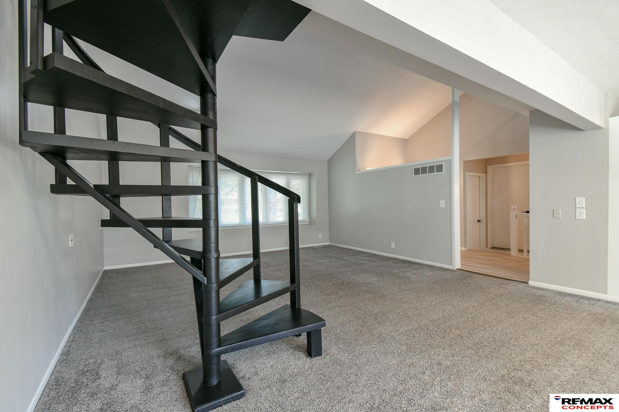 Empty living room with gray carpet, a black spiral staircase, and a high vaulted ceiling.