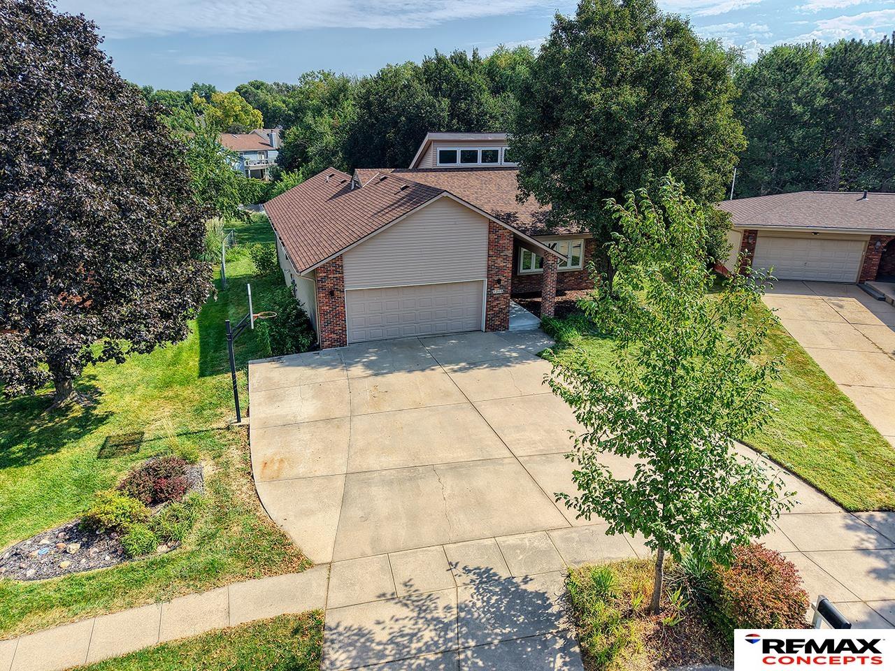 Aerial view of a brick-and-siding home with a wide driveway, double garage, and mature trees.