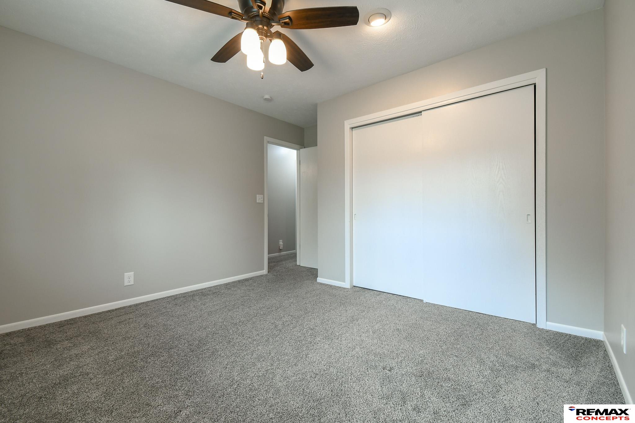 Empty bedroom with gray carpet, a ceiling fan, and large white sliding closet doors.