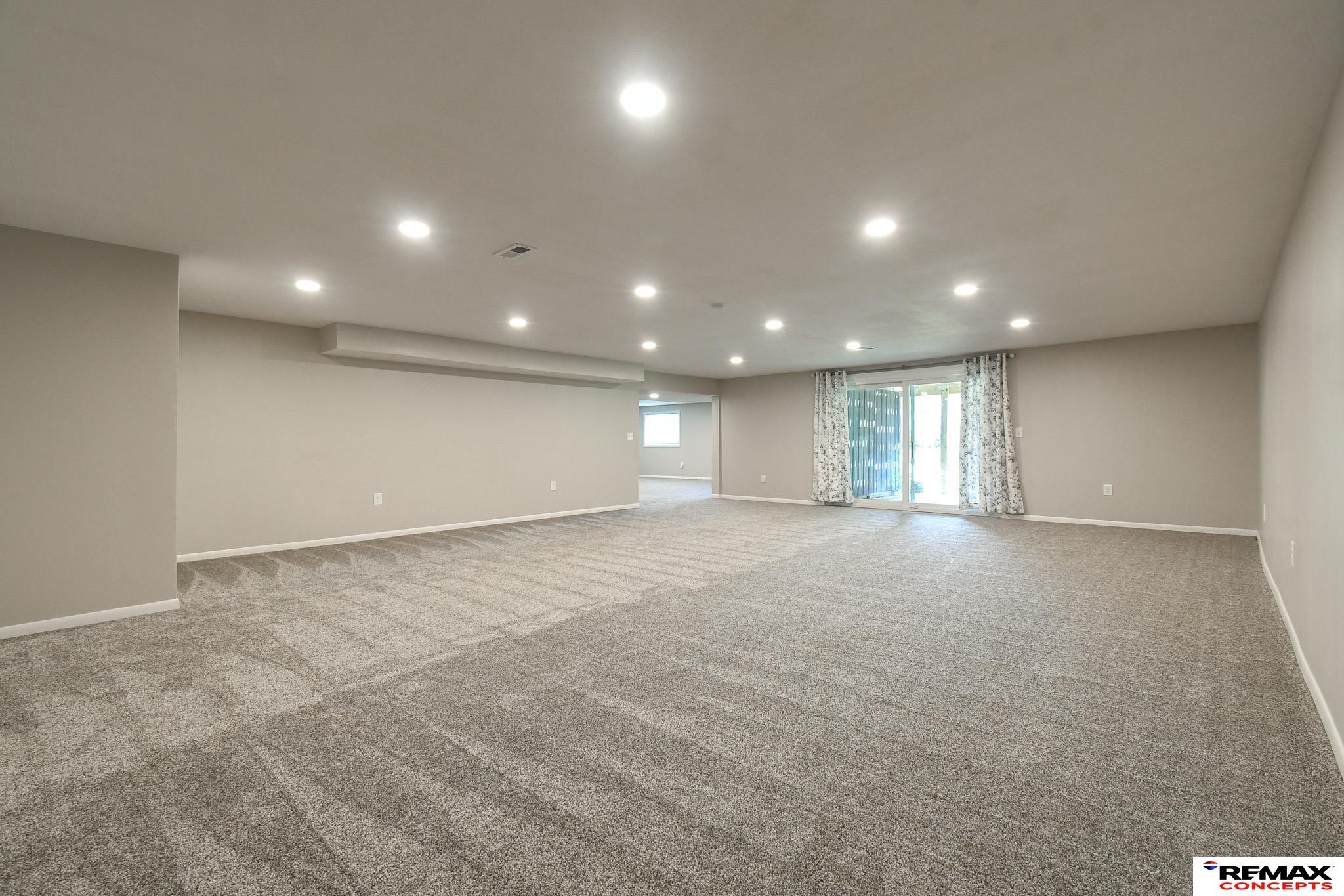 Large empty carpeted room with recessed lights, sliding glass doors, and an opening to an adjoining room.