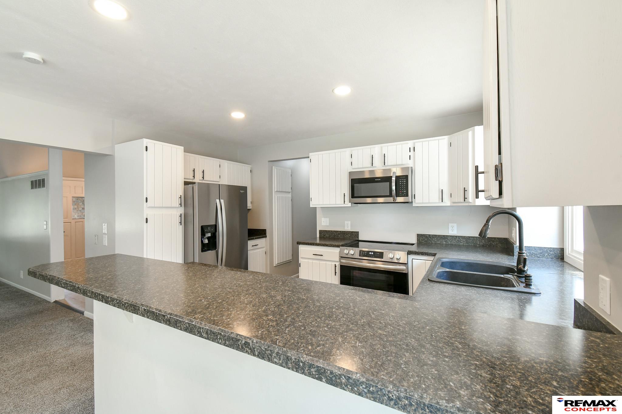 Kitchen with white cabinets, stainless appliances, and a long speckled countertop peninsula.