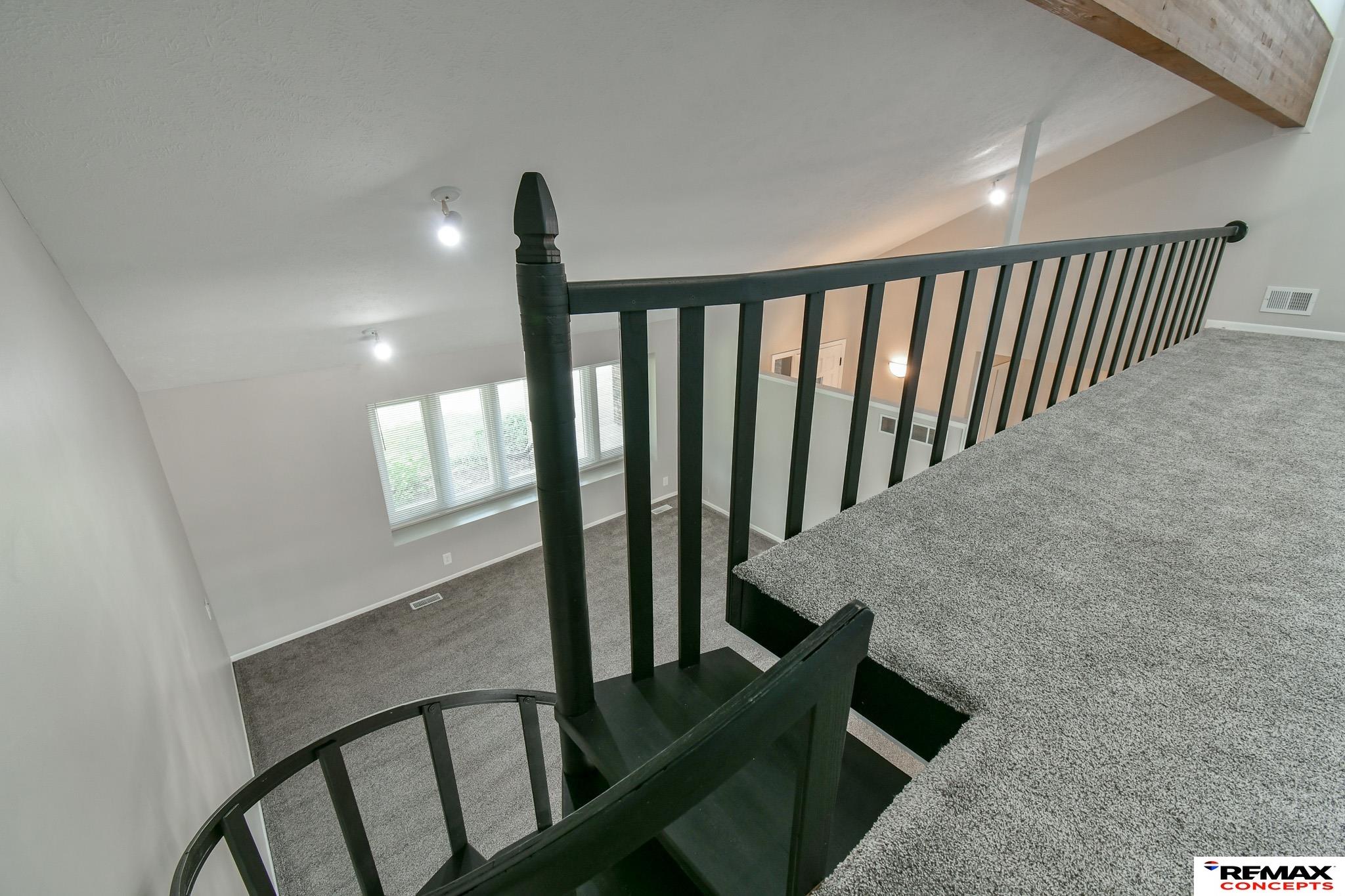Carpeted upper landing overlooking a lower-level room, with a curved staircase and dark railing.