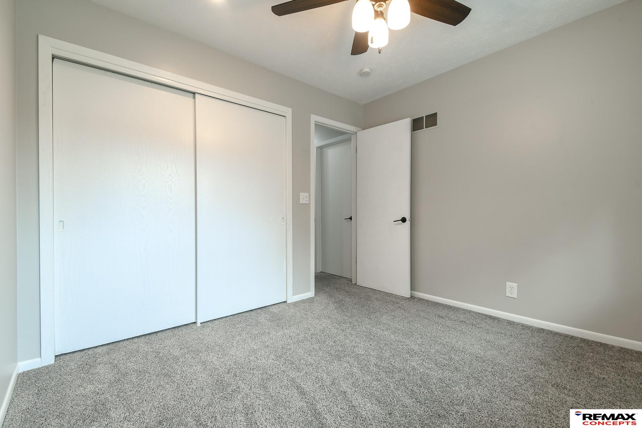 Empty bedroom with gray carpet, a large sliding-door closet, and a ceiling fan.