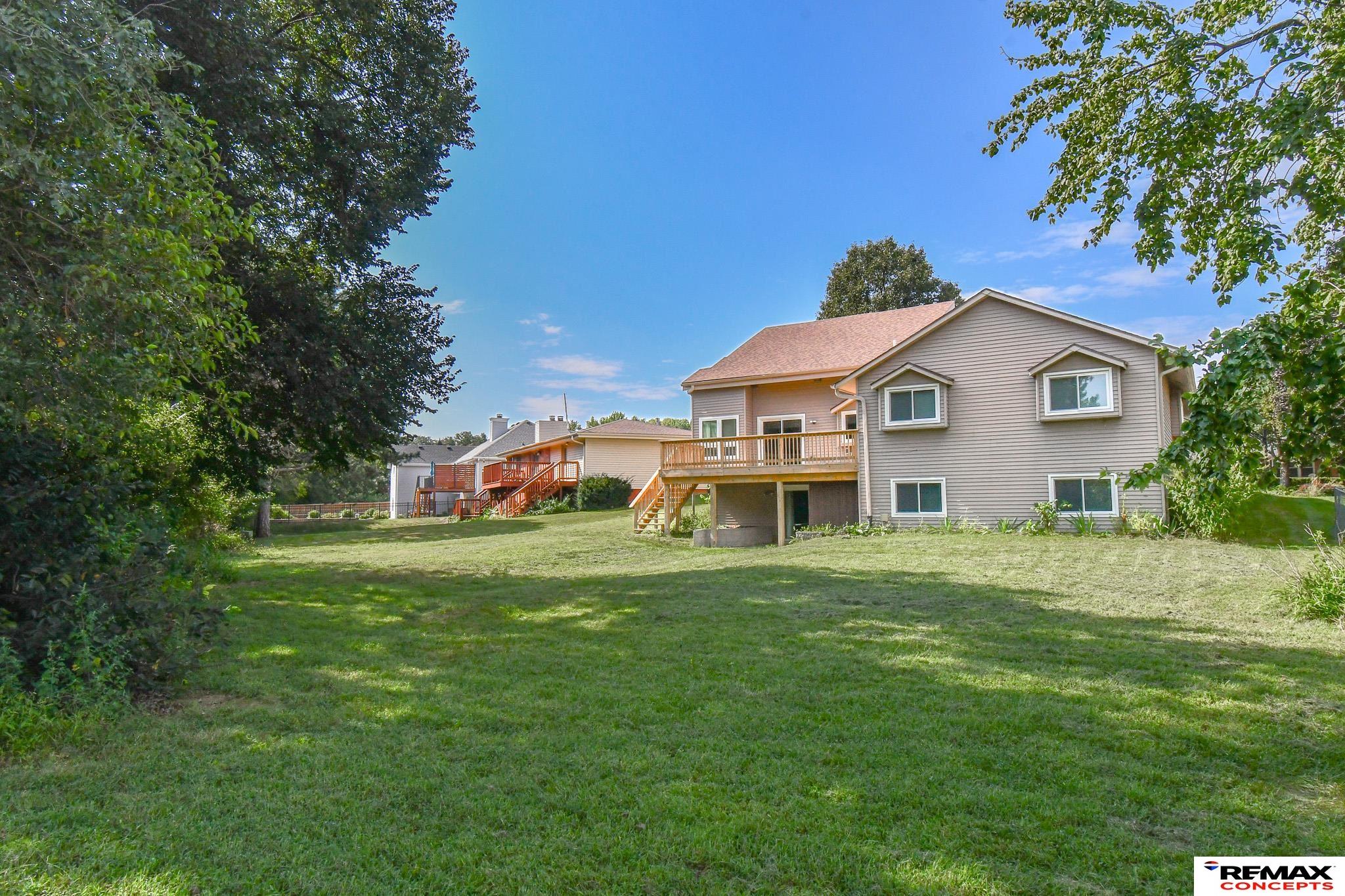 Rear of a gray-sided house with a raised wooden deck overlooking a broad lawn.
