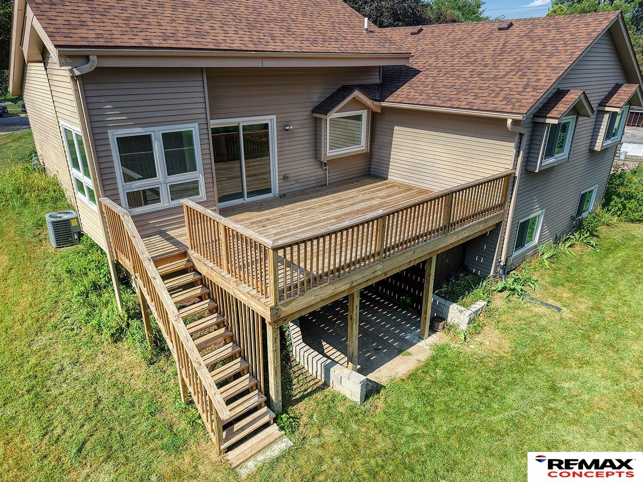 Rear of gray-sided house with a large elevated wooden deck and stairs to the lawn.