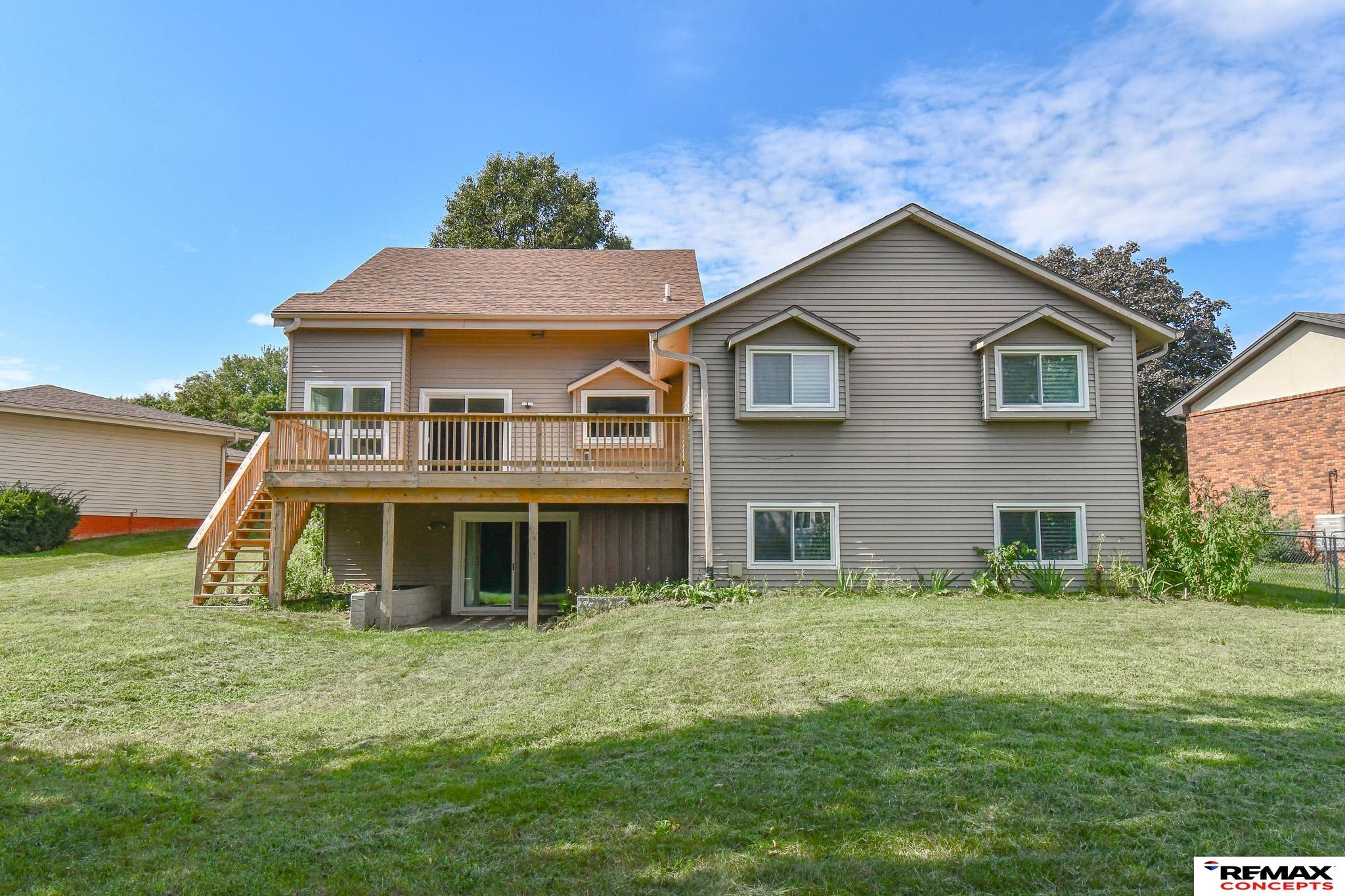 Rear of a gray-sided house with a raised wooden deck and stairs overlooking a grassy backyard.