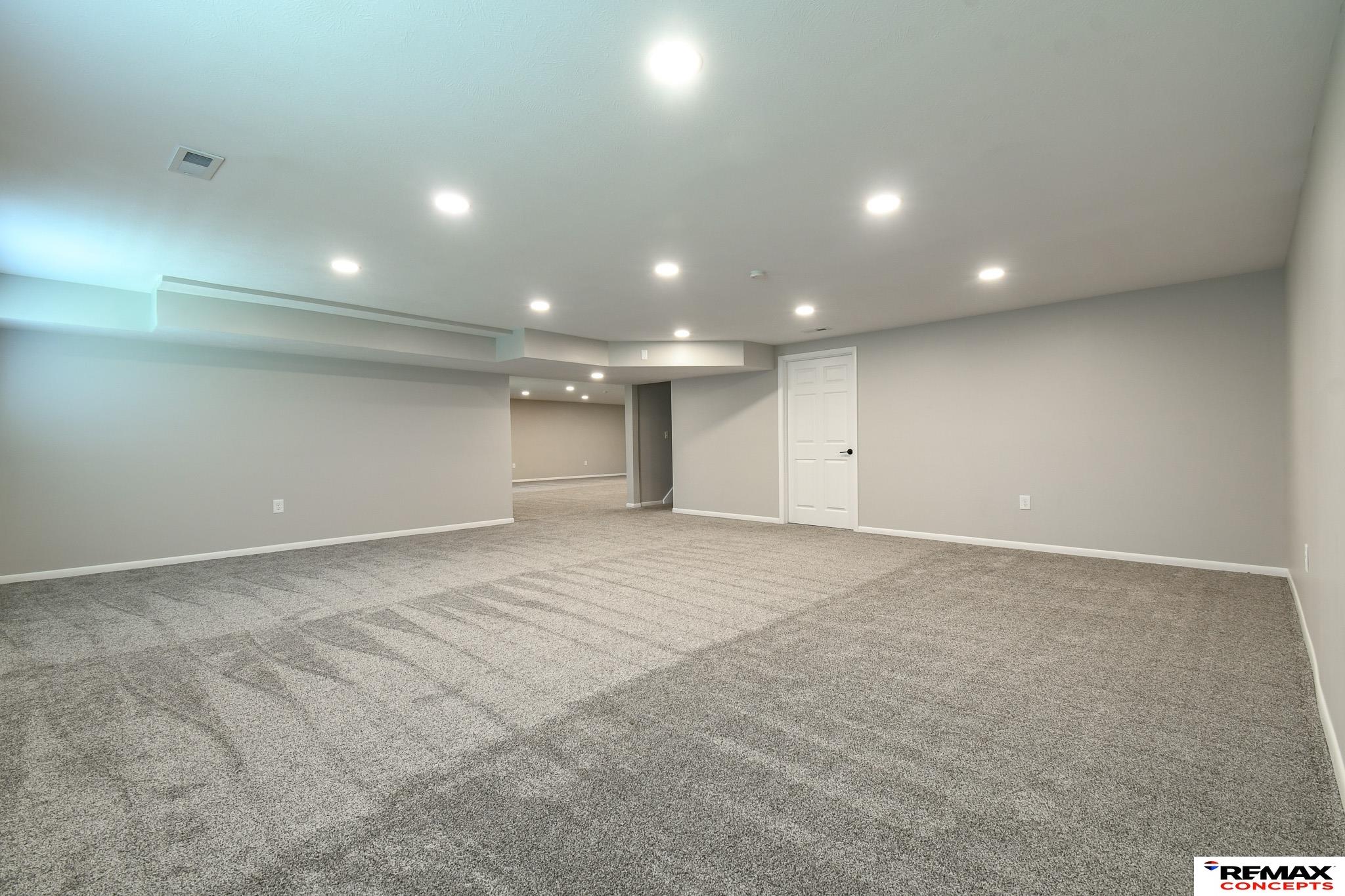 Vacant carpeted basement with recessed lighting and an open passage to another room.