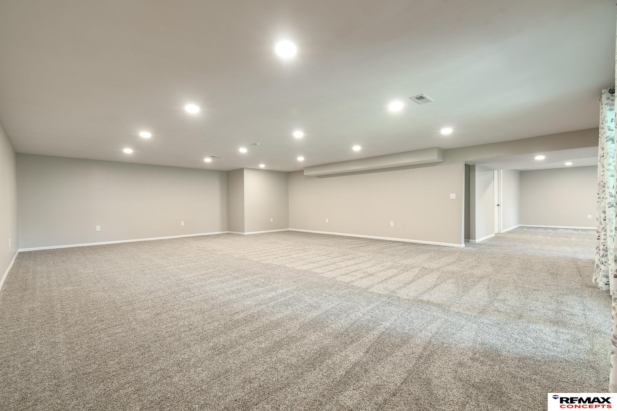 Vacant carpeted room with beige walls, recessed lighting, and a curtained window.