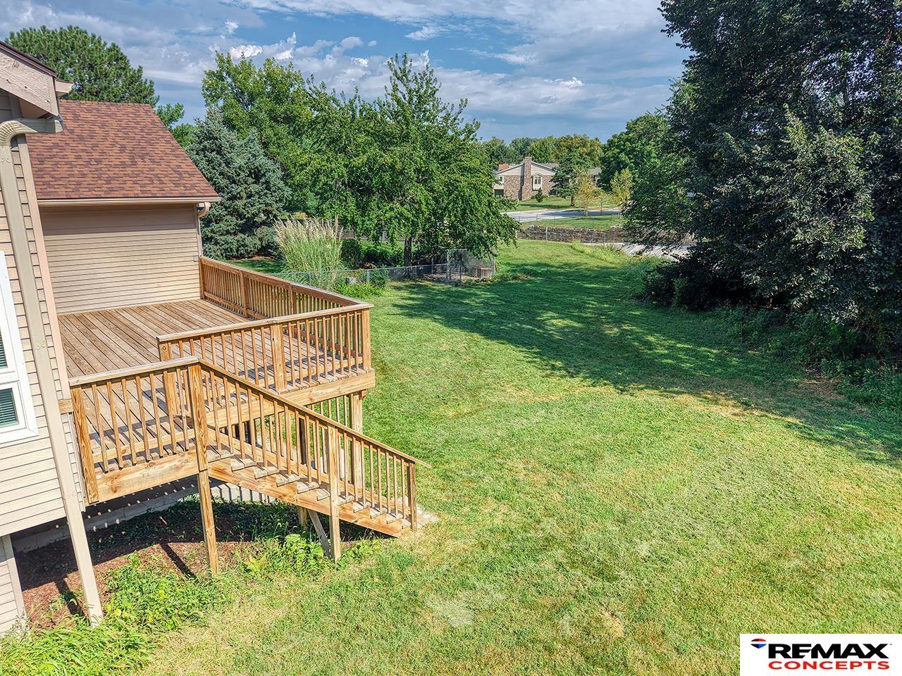 Grassy backyard with a raised wooden deck and stairs beside the house.