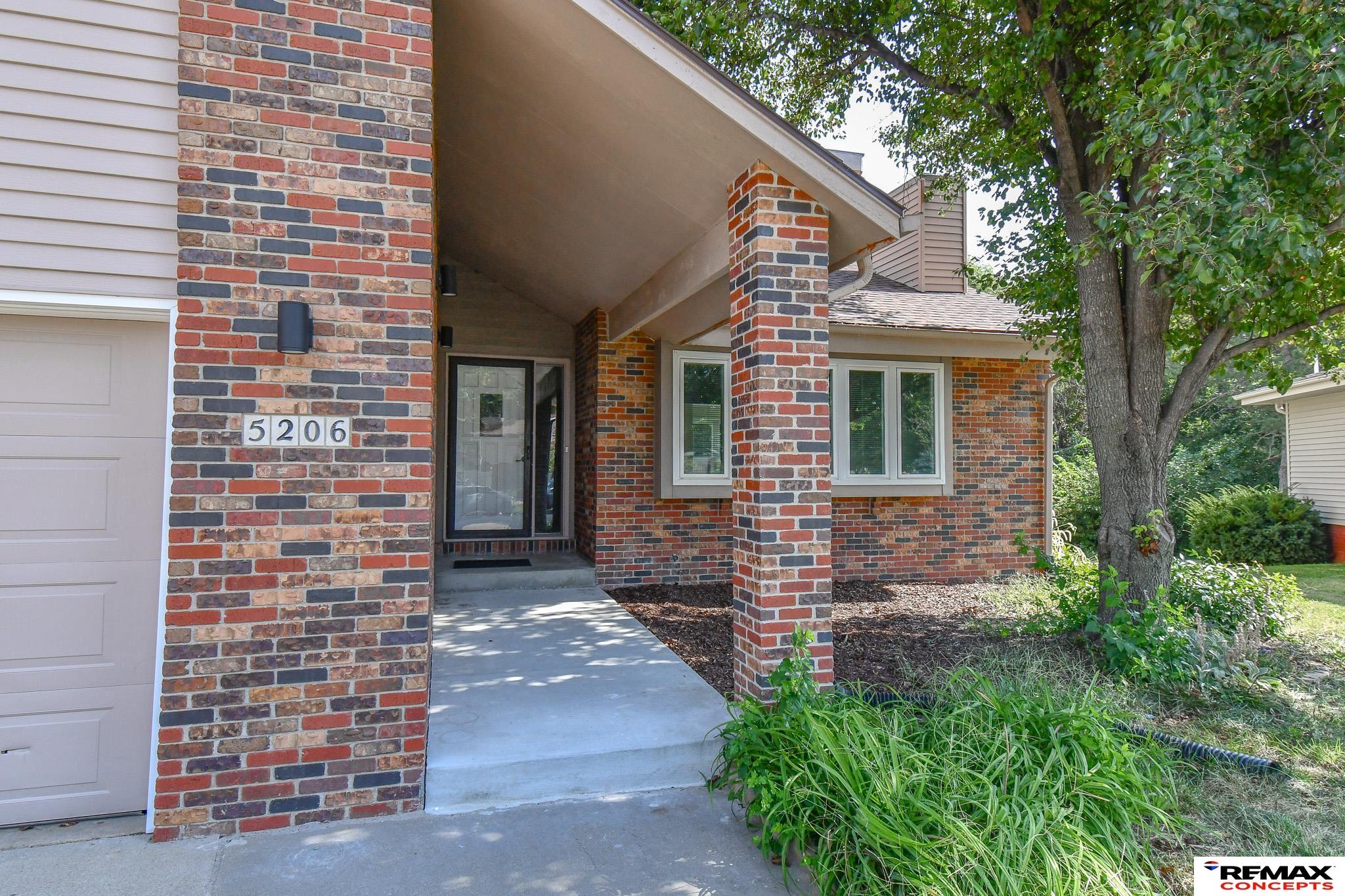 Brick home entrance with a covered porch, white garage door, and landscaped garden beds.