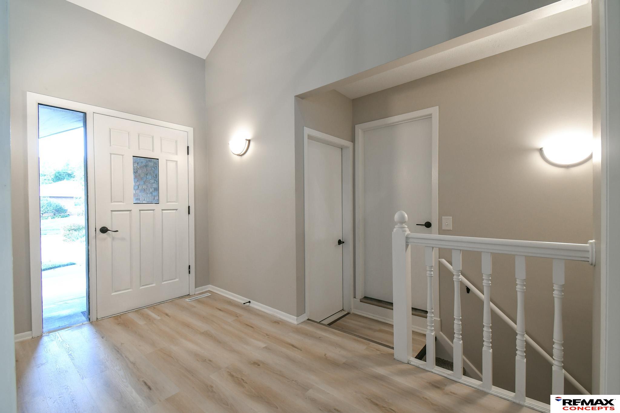Entry foyer with vaulted ceiling, light wood floors, white front door, and staircase railing