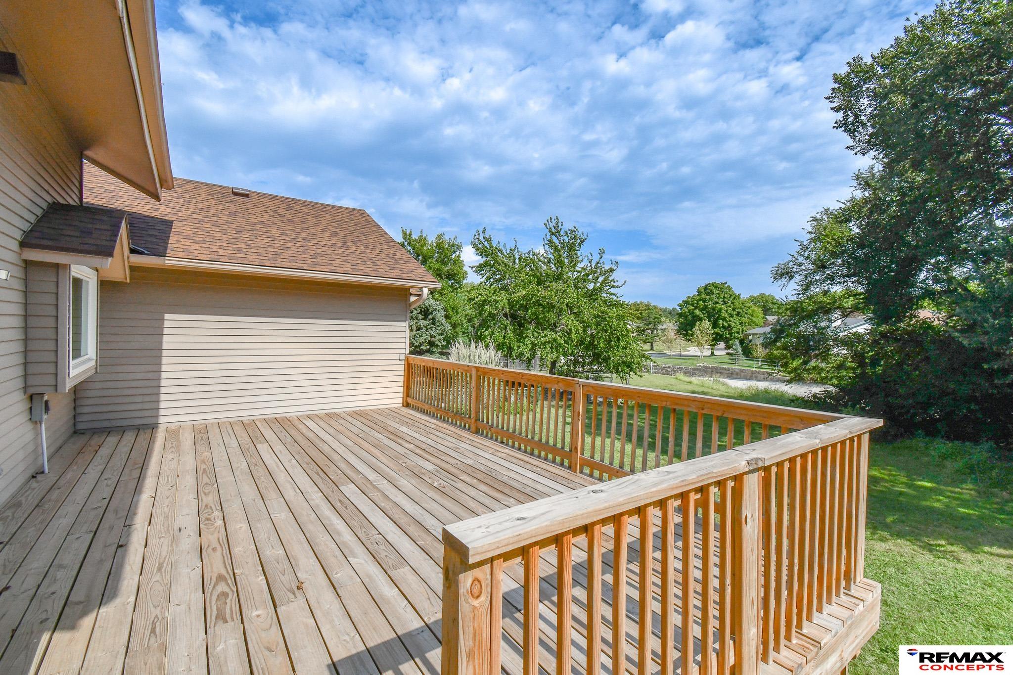 Raised wooden deck beside a gray-sided home, overlooking a lawn and mature trees.