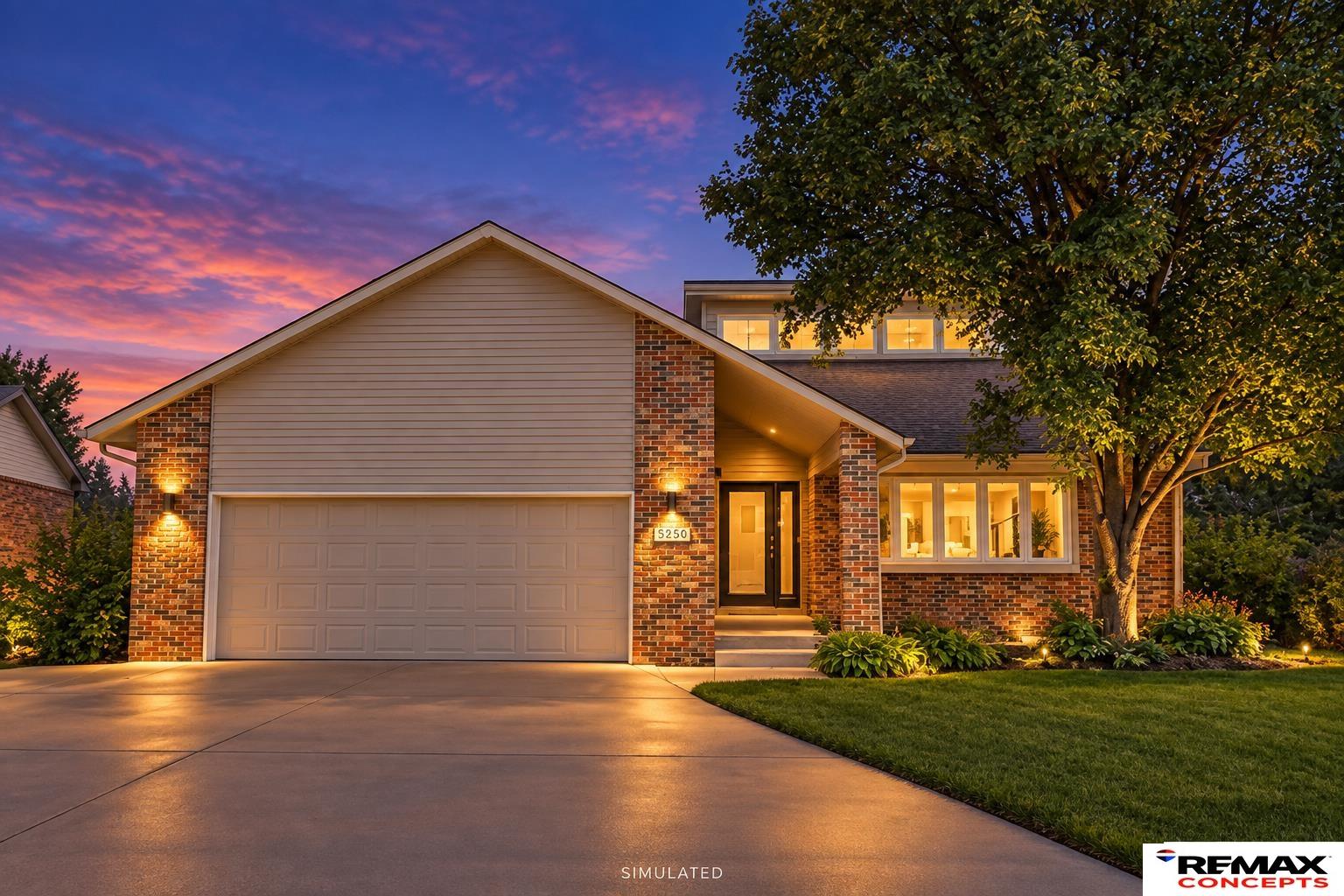 Brick-and-siding home with an attached garage and illuminated landscaping at dusk.
