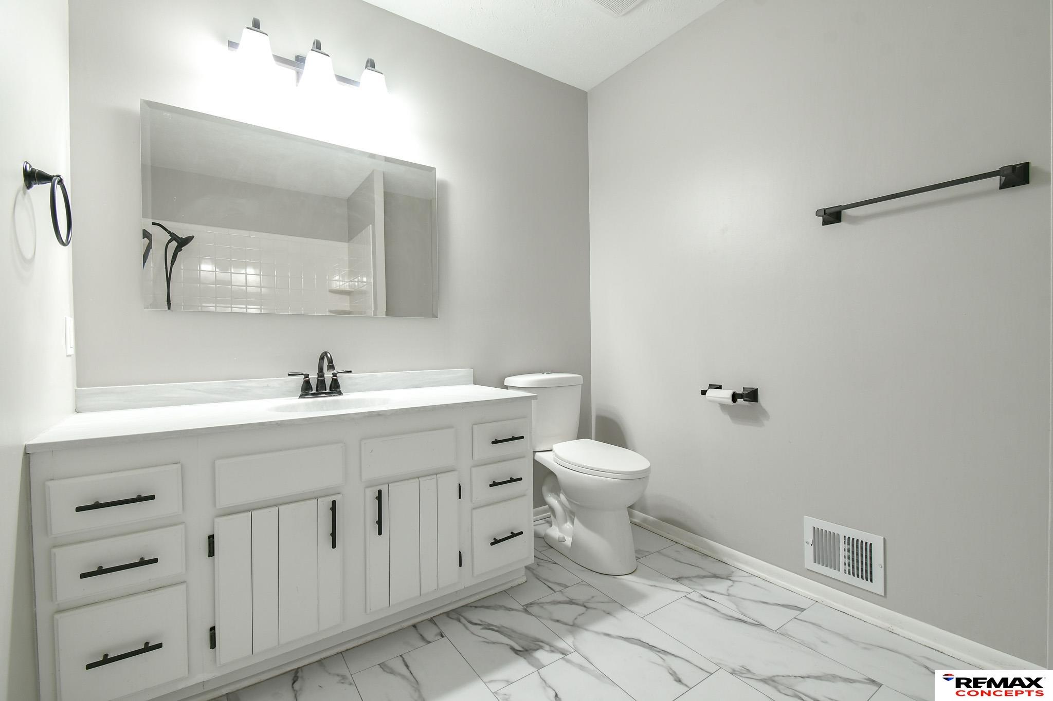 Bathroom with a white vanity, large mirror, toilet, and marble-patterned tile floor.