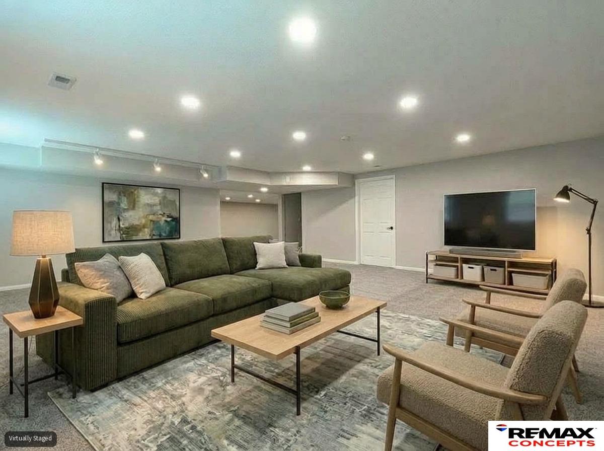 Virtually staged basement living room with a dark green sectional, two chairs, and a television.