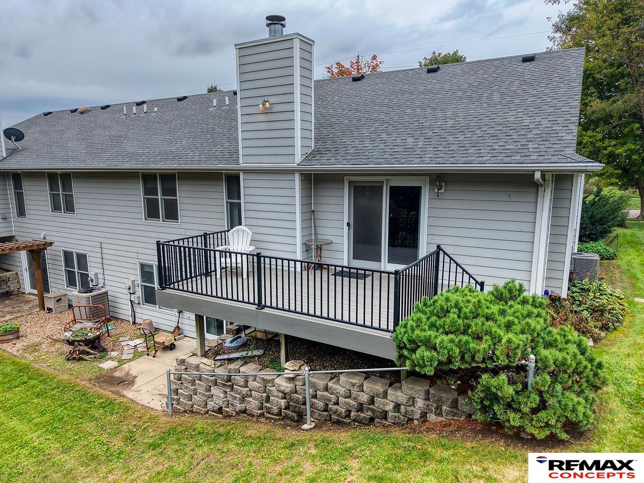 Rear of a gray-sided house with an elevated black-railed deck and white chair.