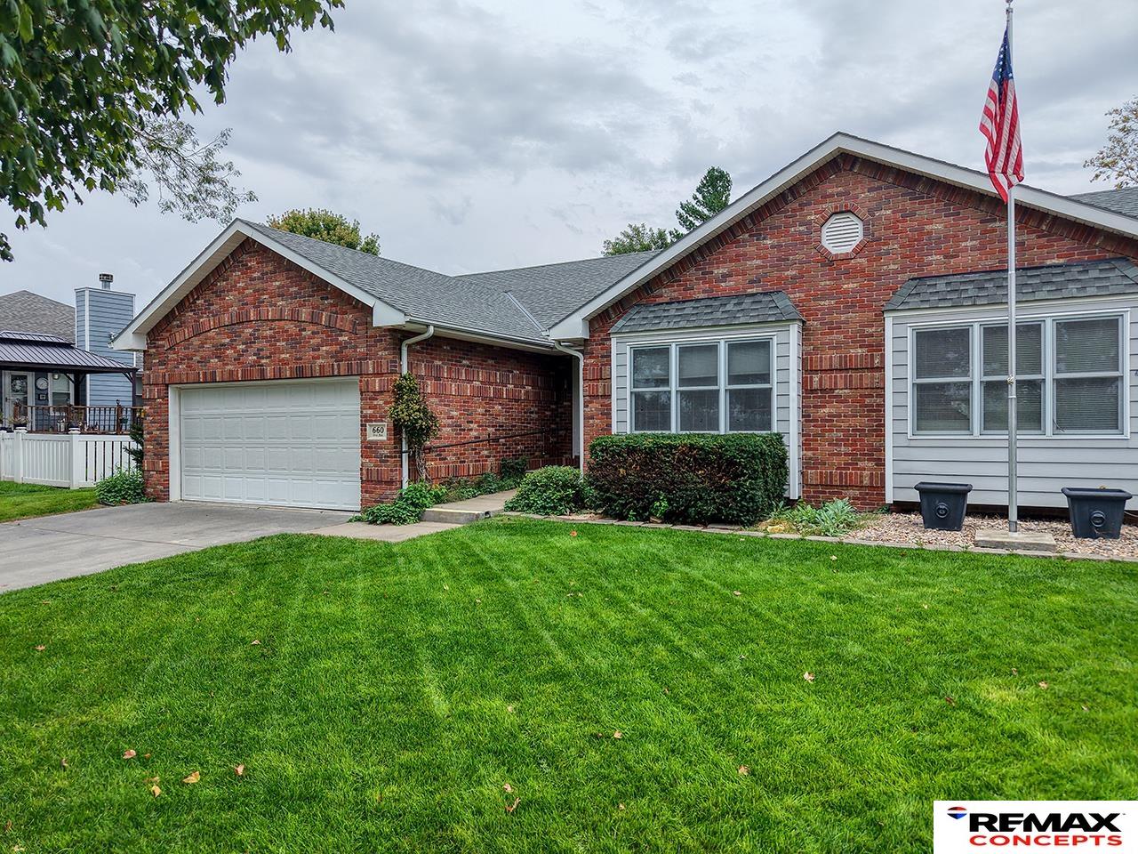 Red brick home with an attached garage, broad lawn, and an American flag.