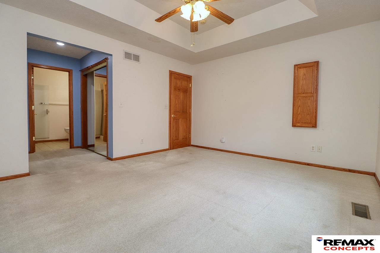 Empty bedroom with a tray ceiling, wood ceiling fan, and doorway to a bathroom and mirrored closet.