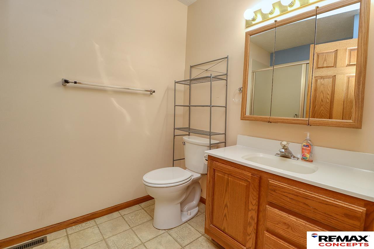 Bathroom with a wood vanity, white sink and toilet, mirrored cabinet, and tiled floor.