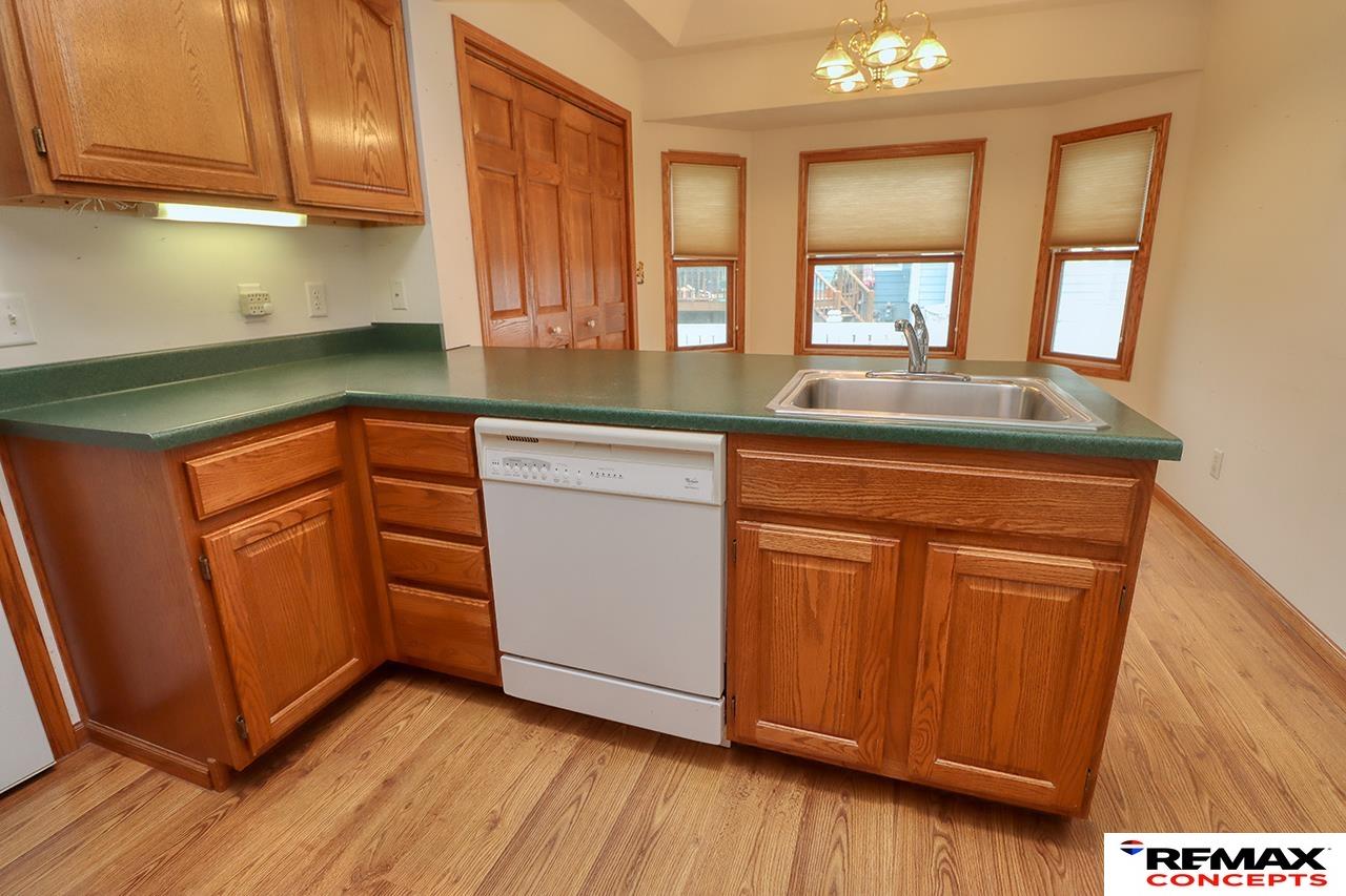 Kitchen with oak cabinets, green countertops, a sink beneath three windows, and wood-look flooring.