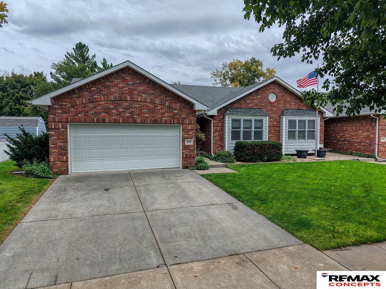 Brick ranch-style home with attached two-car garage, broad driveway, and American flag.