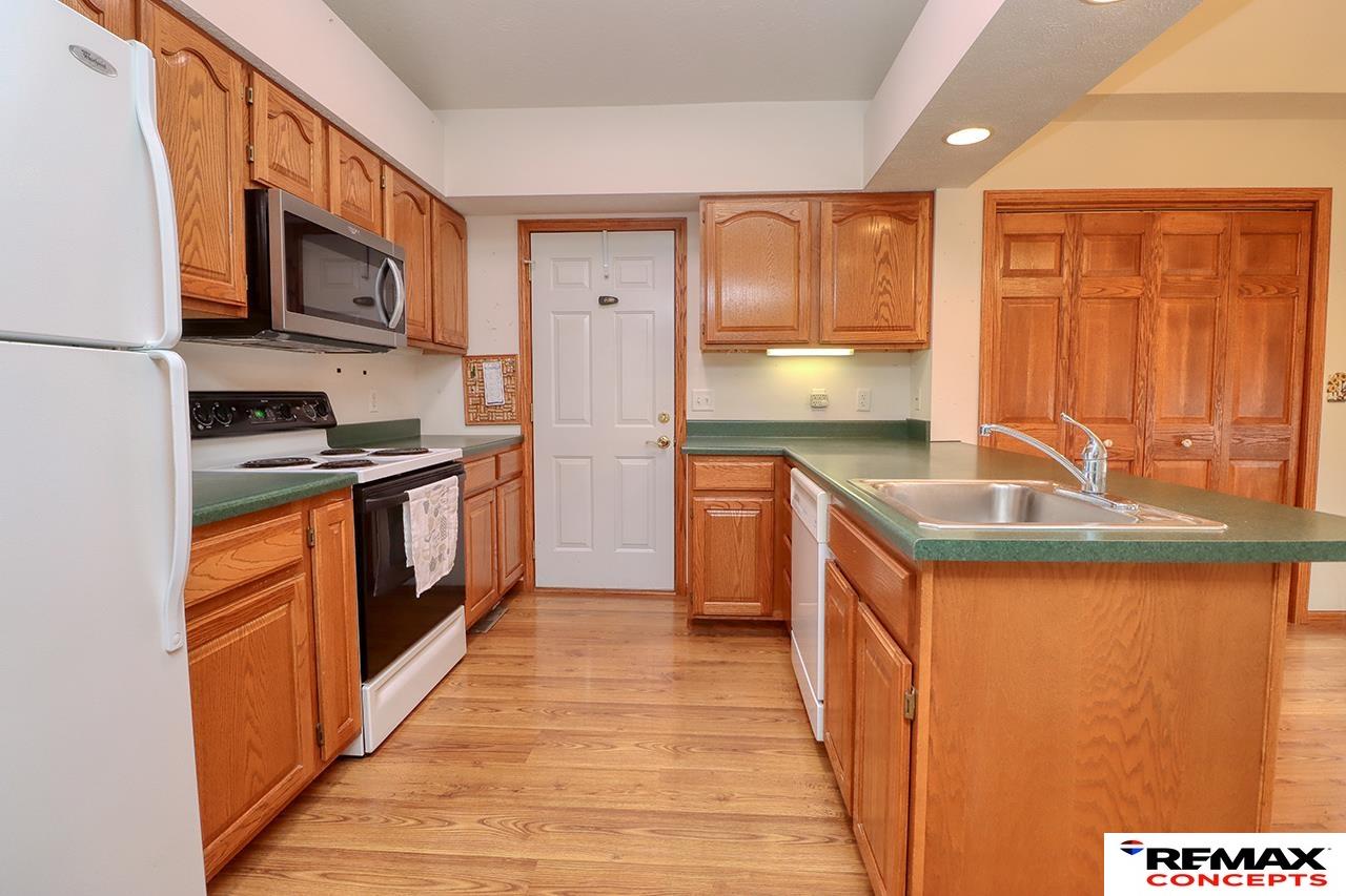 Kitchen with wood cabinetry, green countertops, hardwood floors, and a central island sink.
