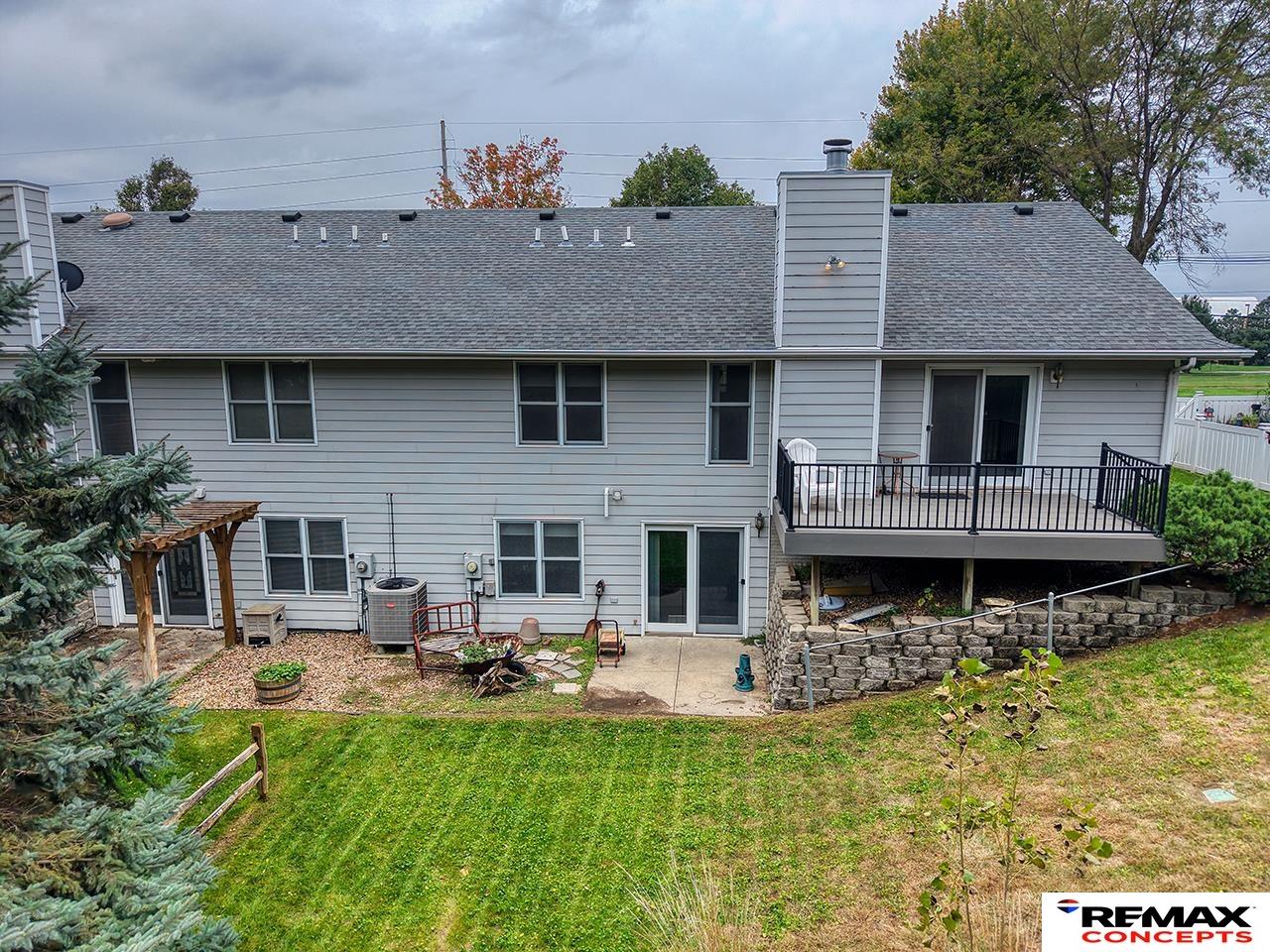 Rear exterior of a gray-sided home with a raised deck, patio, and landscaped yard.