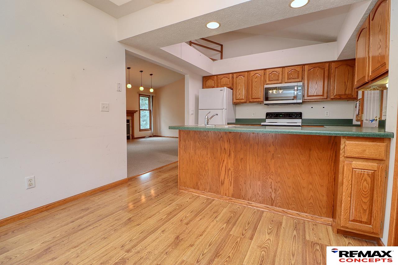 Kitchen with wood cabinets, green counters, white appliances, and hardwood floors opening to a living area.