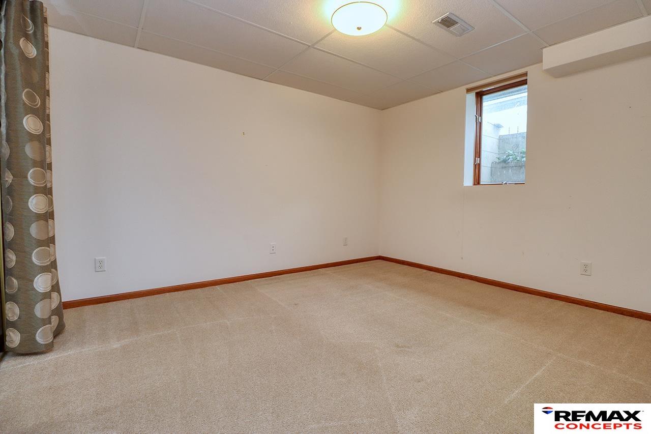 Empty carpeted room with a small high-set window and patterned curtain.