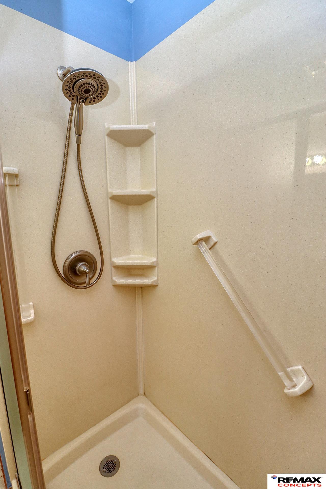 Beige shower stall with built-in corner shelves and a handheld showerhead.