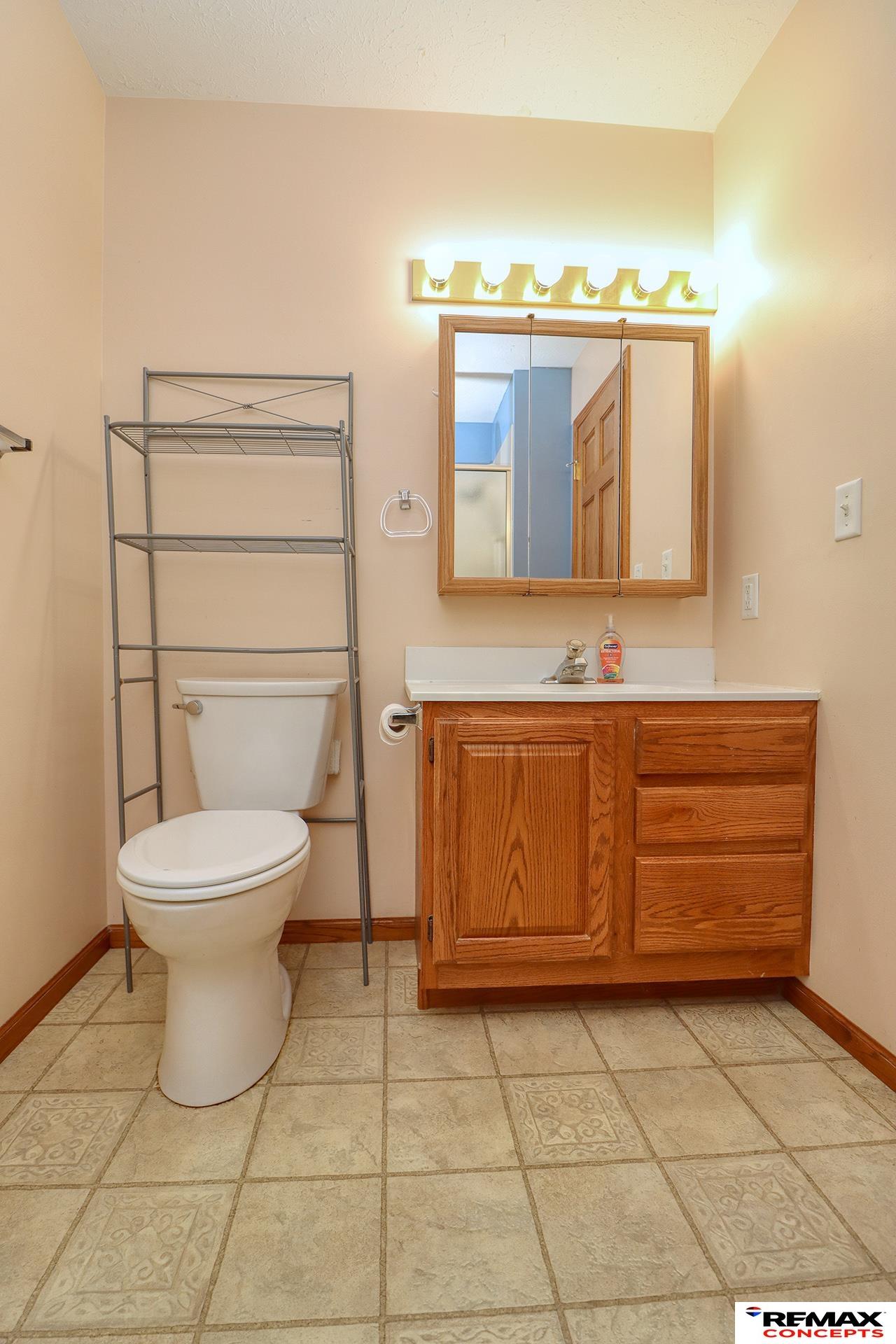 Bathroom with an oak vanity, mirrored medicine cabinet, white toilet, and patterned tile floor.