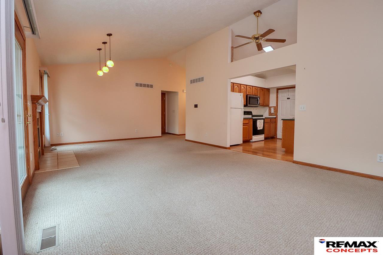 Vacant living room with a wood-trimmed fireplace, carpeted floor, and an open kitchen.