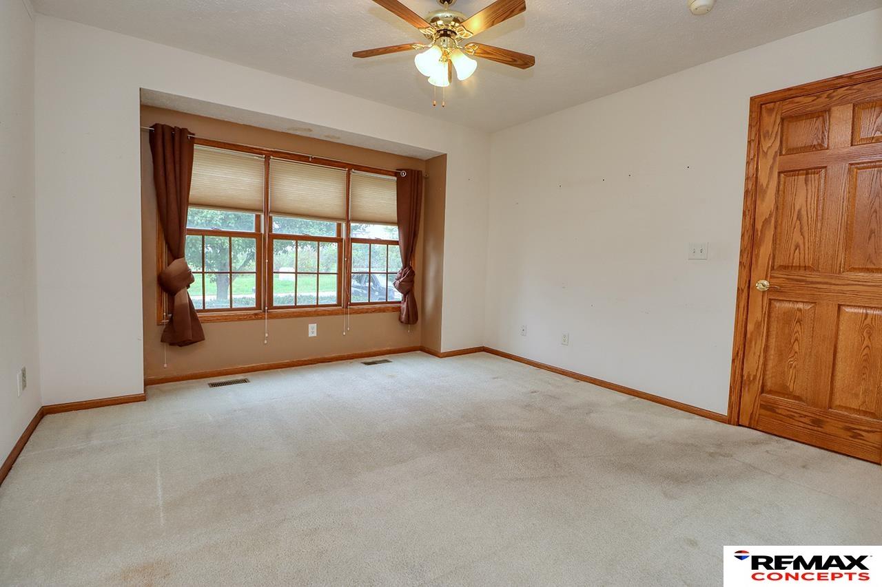 Empty carpeted bedroom with curtained windows, a wooden door, and a ceiling fan.